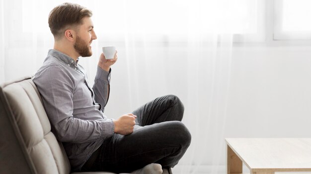 Side view man on couch drinking coffee