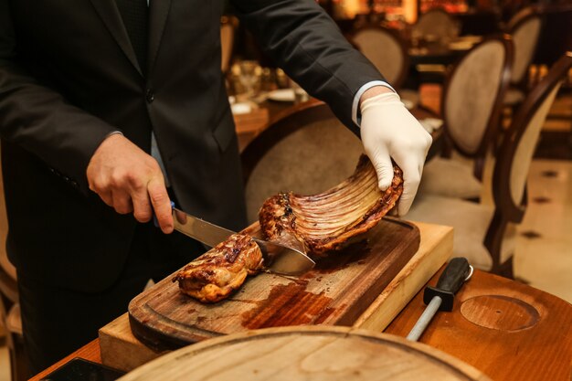 Side view man cuts fried meat ribs on a cutting board