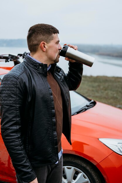 Side view of man drinking next to car