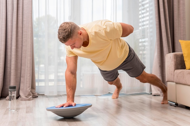 Free photo side view man exercising at home using bosu ball