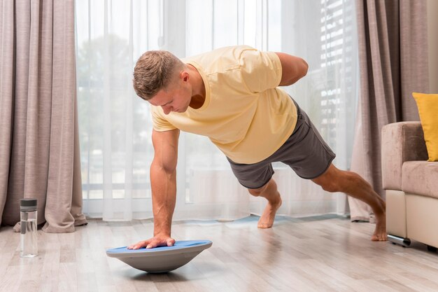 Side view man exercising at home using bosu ball