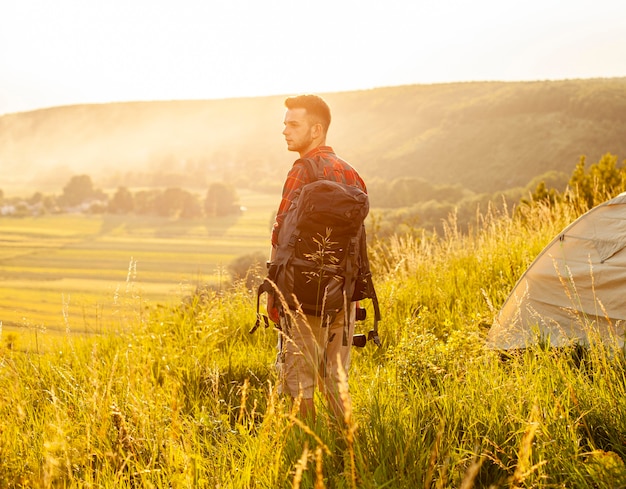 Side view man in green field with backpack