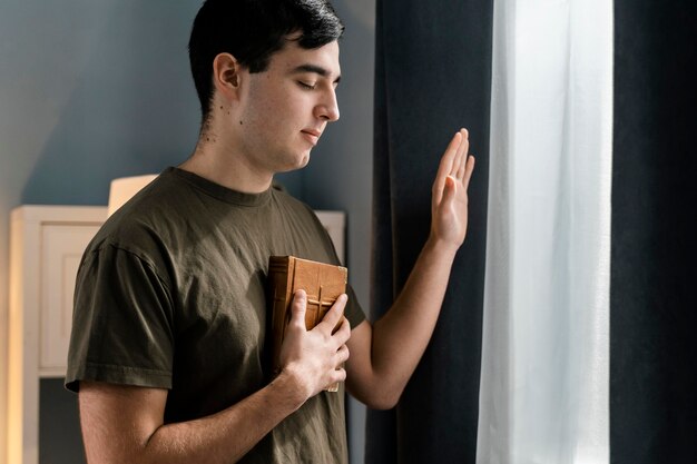Side view of man holding the bible while sitting next to window