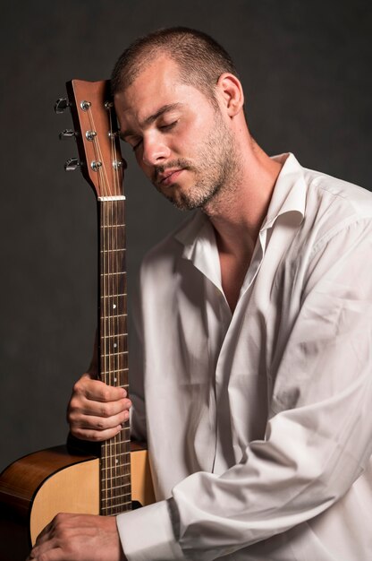 Вид сбоку мужчина держит голову на грифе гитары
