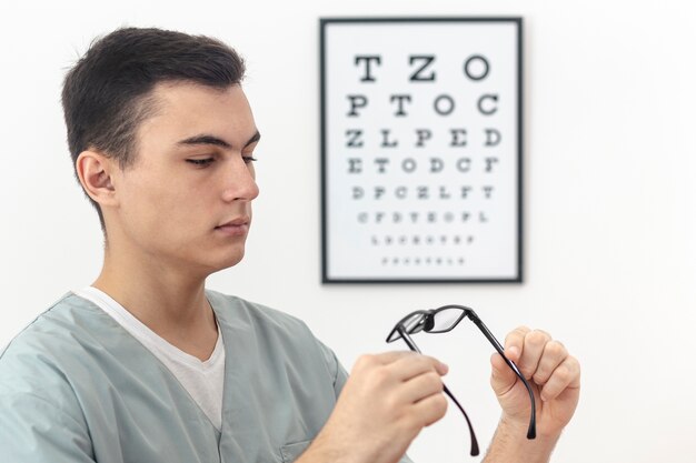 Side view of man holding and looking at pair of glasses