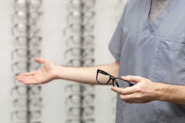 Side view of man holding pair of glasses in hand and showing other pair with the other hand