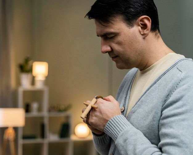 Вид сбоку человека, держащего деревянный крест и молящегося