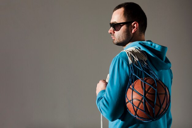 Вид сбоку человека в балахон, держа баскетбол в сети с копией пространства