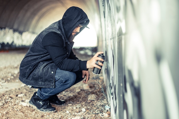 Side view of a man in hoodie painting on graffiti wall