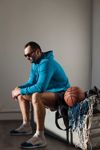 Side view of man in hoodie and sunglasses with basketball next to him