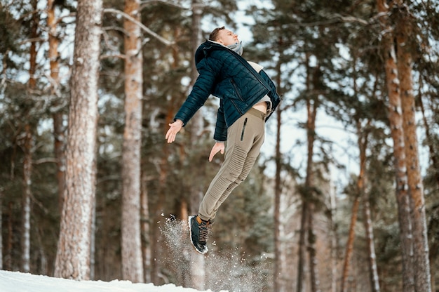 冬の間に自然の中で屋外ジャンプする男の側面図