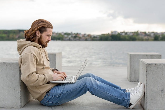 Вид сбоку человека рядом с озером работает на ноутбуке
