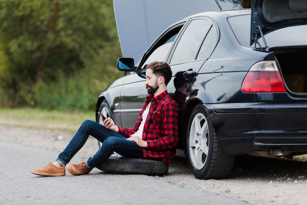 Free photo side view of man leaning on car