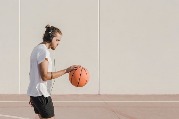 Free photo side view of a man listening to music while practicing basketball