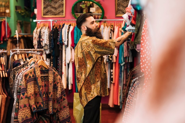 Вид сбоку человека, смотрящего на одежду, висящую на рельсе в магазине