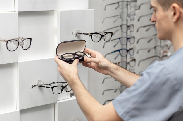 Side view of man looking at pair of glasses in hands