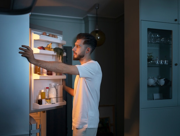 Side view man looking for snacks in the fridge