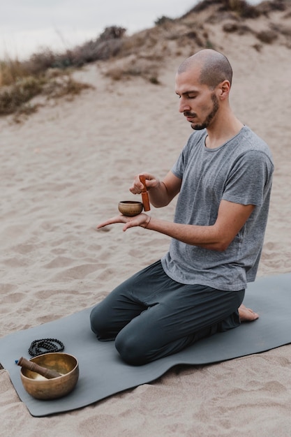 Side view of man on mat outdoors with singing bowl