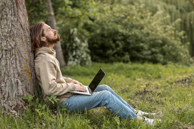 Free photo side view of man in nature with laptop