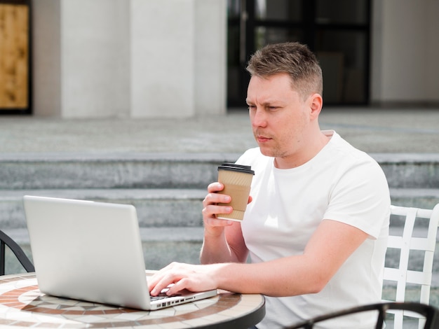 屋外でコーヒーを飲んでいるとラップトップに取り組んでいる男の側面図