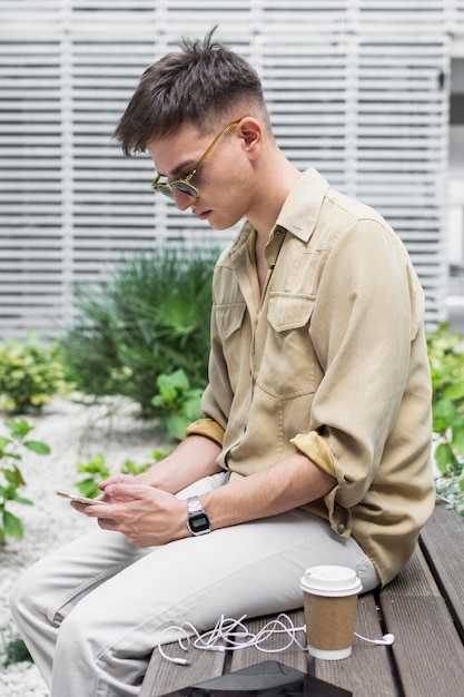 Side view of man outdoors looking at smartphone and having coffee