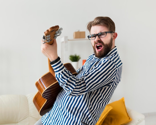 Side view of man playing guitar at home