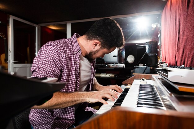 Side view man playing the keyboard in the studio