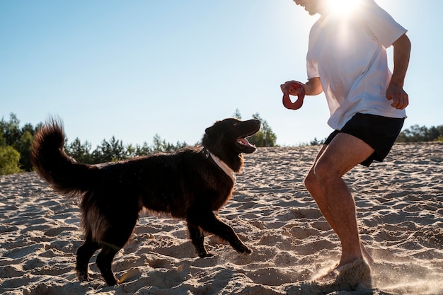 Foto gratuita uomo di vista laterale che gioca con il cane in spiaggia