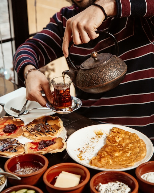 측면보기 남자는 테이블에 차 아침 팬케이크와 스크램블 계란을 부 어