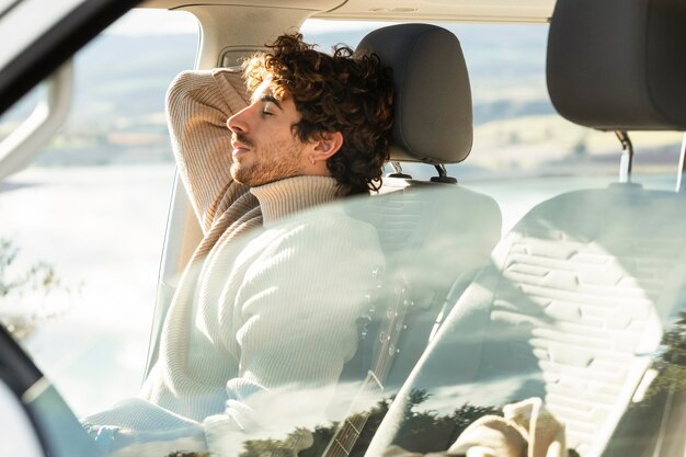 Side view of man relaxing in car while on a road trip
