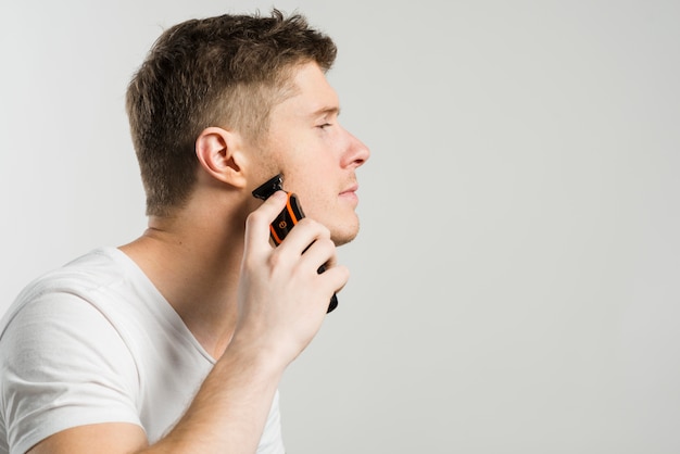 Side view of a man shaving stubble with an electric razor isolated over gray background