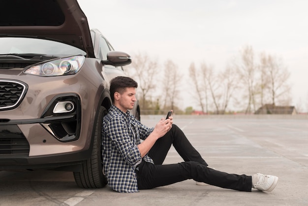 Foto gratuita uomo di vista laterale che si siede accanto all'automobile rotta