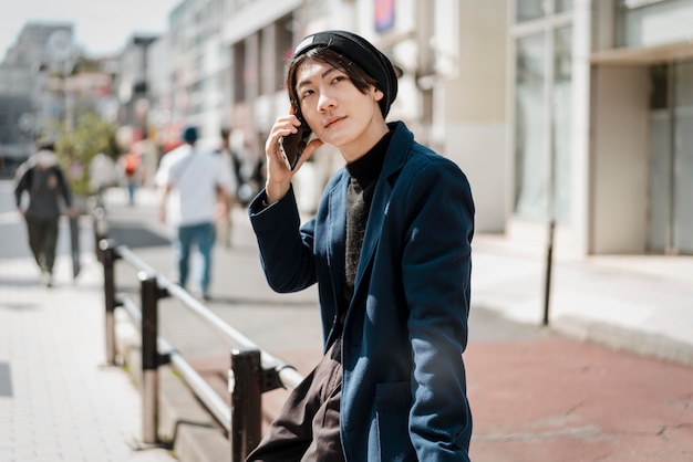 Side view of man sitting on railing and talking on the phone