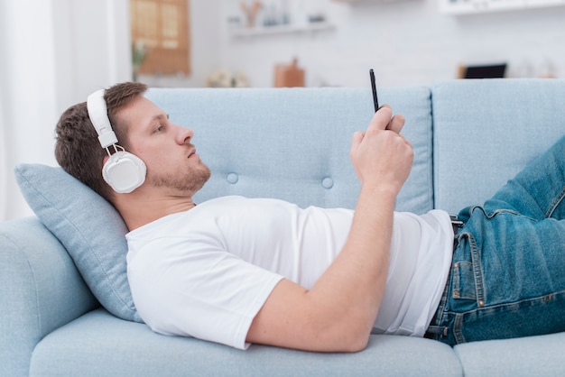 Side view man staying on the couch and looking on his phone