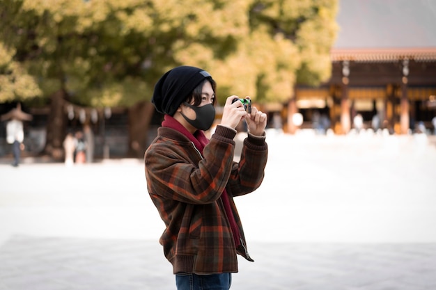 Free photo side view of man taking pictures outdoors while wearing face mask