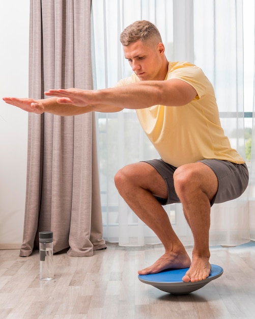 Side view man training at home using bosu ball