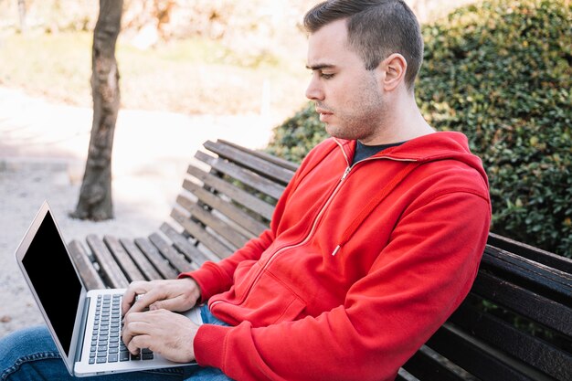 Side view man using laptop on bench