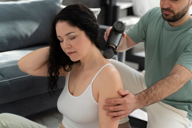 Side view man using massage gun on woman