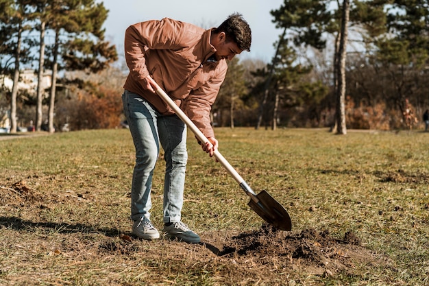 Вид сбоку на человека, использующего лопату, чтобы вырыть яму для посадки дерева