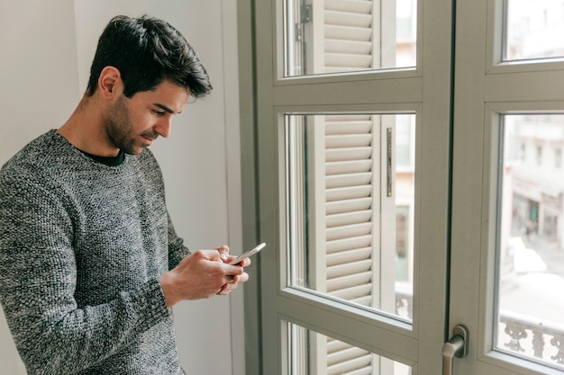 Side view man using smartphone near window