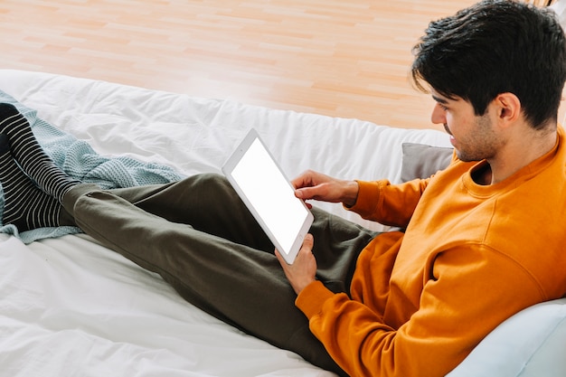 Вид сбоку человек, используя планшет на кровати