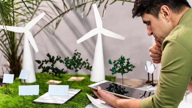 Foto gratuita vista laterale dell'uomo che utilizza tablet accanto a un layout di progetto di energia eolica eco-compatibile