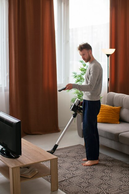 Side view man vacuuming and watching tv