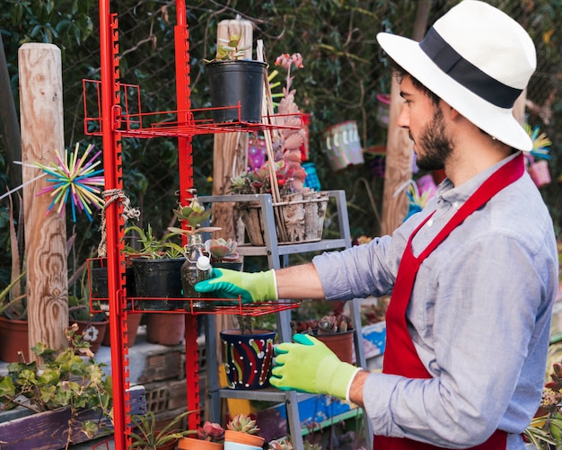 Side view of a man wearing gloves arranging the potted plants in the red rack