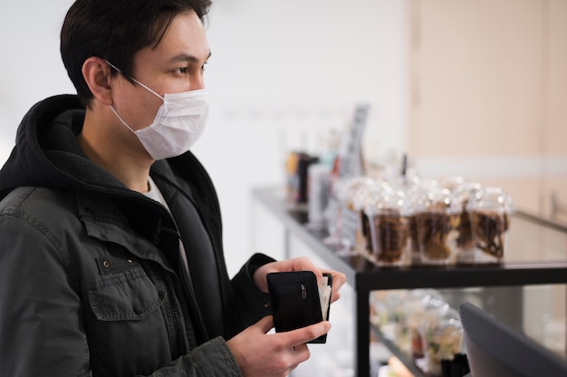 Foto gratuita vista laterale dell'uomo che indossa maschera medica che compra qualcosa