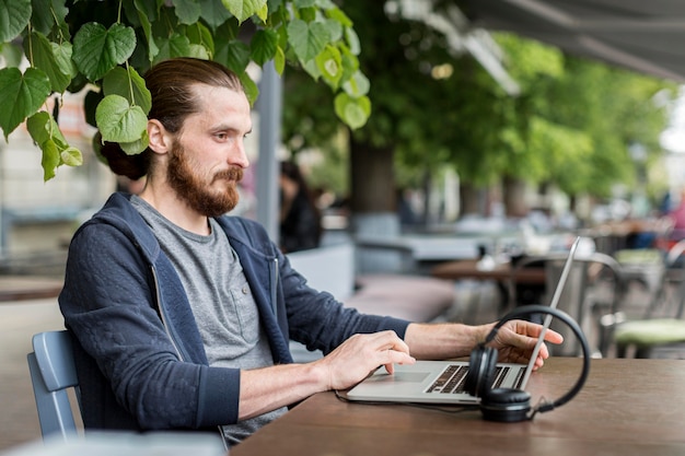 Side view of man with laptop and headphones at city terrace