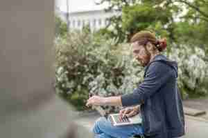 Free photo side view of man with laptop outdoors in the city