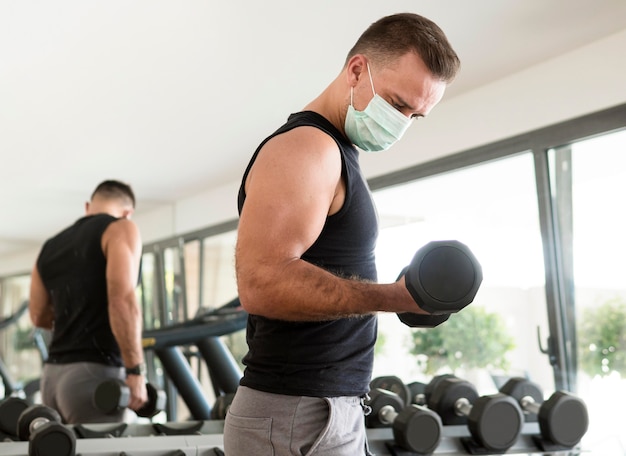 Free photo side view of man with medical mask exercising at the gym