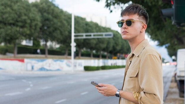 スマートフォンを持って街でサングラスをかけた男の側面図