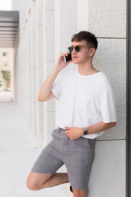 屋外の電話で話しているサングラスを持つ男の側面図